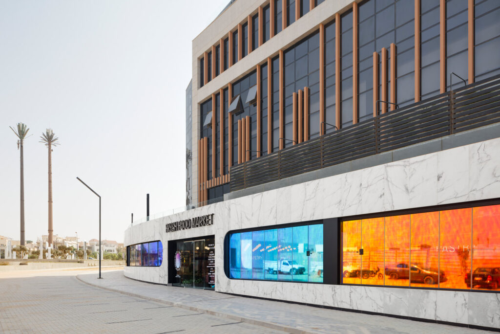 Fassade des Fresh Food Market aus hellem Marmor und farbig foliierter Fensterfront.